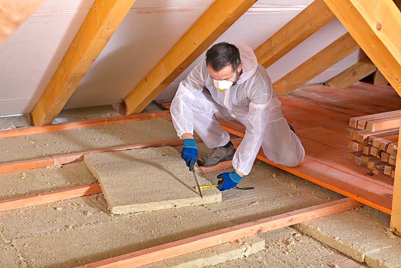 man cuts loft insulation boards in roof